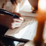 crop author writing novel in copybook with feather in sunshine