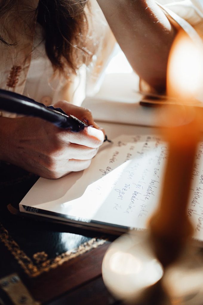 crop author writing novel in copybook with feather in sunshine